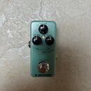 Zelený efekt pedál s nápisy SUSTAIN, ATTACK a LEVEL u ovládacích knoflíků. Uprostřed je uveden název HYPERGRAVITY a pod ním text MINI COMPRESSOR, ve…