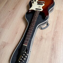 Elektrická kytara s hnědým sunburst povrchem korpusu a bílým pickguardem, umístěná v černém tvrdém kufru. Na hlavě hmatníku je zlatý nápis Epiphone.…