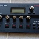 Černý kytarový efektový procesor s nápisy BOSS a GUITAR EFFECTS PROCESSOR GT-001. Zařízení má v horní části displej, pět stříbrných otočných ovladačů…