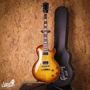 Elektrická kytara s žlutohnatým sunburst povrchem a dvěma humbuckery. Na hlavě hmatníku je nápis Gibson a modelové označení Les Paul Model. Kytara je…