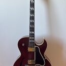 Tmavě červená polodublová elektrická kytara s gold hardwarem a bílým lemováním. Na hlavě je nápis Gibson a logo v podobě koruny. Tělo má dva humbucke…