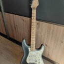 Stříbrná elektrická kytara typu Stratocaster s bílým perleťovým pickguardem a javorovým hmatníkem. Na hlavě je černý nápis Fender STRATOCASTER. Nástr…