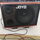 Kytarový kombo zesilovač s hnědým povrchem v imitaci kůže a černou kovovou mřížkou. Na mřížce je bílý nápis JOYO. Horní panel obsahuje ovládací knofl…