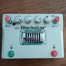 Stříbrný kytarový efekt s nápisy Blackstar a HT-DUAL. Na horní straně jsou čtyři modré otočné knoflíky s popisky BASS, MIDDLE, TREBLE a LEVEL a dva č…