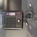 Černý kontrolér s mřížkou 16 padů, umístěný na černém přenosném pouzdře. Na zařízení je v horní části nápis MPC STUDIO a logo AKAI PROFESSIONAL. Vedl…