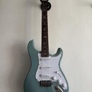 Modrošedá elektrická kytara s bílým pickguardem a třemi snímači. Na hlavě hmatníku je viditelné logo "Epiphone". Hmatník je tmavého dřeva s ptačími i…