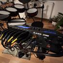 Elektronická bicí souprava s modulem ALESIS STRIKE. Modul je černý, vybaven displejem a řadou ovládacích prvků s nápisy MIDI OUT, MIDI IN, DISPLAY CO…