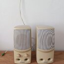 Dva béžové reproduktory s textilními maskami umístěné na dřevěném povrchu. Na spodní části obou reproduktorů je nápis CAMBRIDGE SOUNDWORKS, levý repr…
