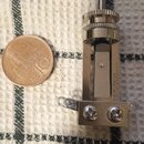 Fotografie zachycuje kovový hudební komponent, pravděpodobně součástku k ladění nebo mechaniku. Na boku je svisle vyražen nápis SWITCHCRAFT. Součástk…