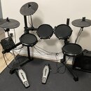 Elektronická bicí souprava s černými pady a činely na černém kovovém rámu. Na modulu je nápis ALESIS TURBO a na pedálech značka ALESIS. Součástí je č…