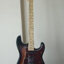 Elektrická kytara s trupem v tmavě hnědém sunburst provedení a hmatníkem ze světlého dřeva. Na hlavě je vidět nápis "Bacchus". Kytara má červený želv…