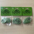 Tři uzavřená balení kytarových trsátek v zelené barvě. Na každém zeleném kartonovém podkladu je nápis STANDARD .88 MM, 12 PACK a logo TORTEX. V průhl…