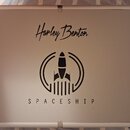 Stříbrný obdélníkový kufr s kovovými hranami a rohy. Na víku je černý nápis Harley Benton a pod ním grafika rakety v kruhu s textem SPACESHIP. Povrch…