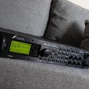 Černý rackový procesor s nápisem FRACTAL AUDIO SYSTEMS a označením modelu Axe-Fx II. Zařízení má digitální displej, na kterém je vidět text PRESET/EF…