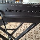 Záběr na zadní panel černého klavíru s řadou konektorů. Jsou zde nápisy DC IN USE ROLAND PS-8U ADAPTOR ONLY, INPUT MIC LINE, R, L/MONO, MIC a OUTPUT…