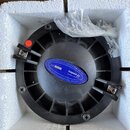 Černý kruhový reproduktor umístěný v polystyrenovém obalu. Na zadní straně je modrý štítek s bílým textem COMPRESSION DRIVER-SMC65/Nd, S.N. A785130,…
