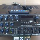Černý zesilovač s nápisem PROFESSIONAL DIGITAL ECHO MIXER POWER AMPLIFIER a značkou Sunbuck, model AV-MP326BT. Zařízení má na předním panelu řadu ovl…