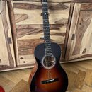 Akustická kytara s tmavě hnědým sunburst povrchem korpusu a černým hmatníkem. Na hlavě nástroje je bílý nápis „Eastman“. Kytara vykazuje známky běžné…