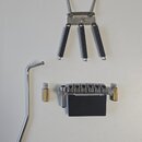 Fotografie zobrazuje sadu komponentů pro kobylku elektrické kytary. Sada obsahuje kovovou základní desku se třemi černými pružinami, samotnou kobylku…