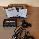 Na fotografii je napájecí zdroj pro efektové pedály Voodoo Lab Pedal Power 2 Plus v černé barvě. K zařízení patří několik černých napájecích kabelů,…