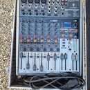 Stříbrný mixážní pult Behringer X2042USB umístěný v otevřeném transportním kufru. Na horní části jsou vidět konektory pro mikrofony, linkové vstupy a…