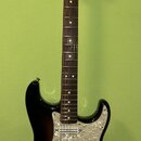 Elektrická kytara s trupem v tmavém sunburst provedení a hnědým hmatníkem. Na hlavě je viditelné logo Fender a nápis STRATOCASTER. Kytara má bílý pic…