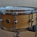 Dřevěný snare buben s přírodním povrchem a chromovaným kováním. Na korpusu je umístěn černý oválný štítek s bílým nápisem HALLVAD drums CZ. Nástroj j…