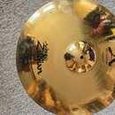 Zlatý kovový činel s viditelným broušením povrchu. Na povrchu jsou nápisy „Avedis Zildjian“ a „A CUSTOM SIZZLE RIDE“, doplněné o velké logo ve tvaru…