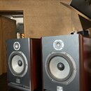 Dva kompaktní reproduktory v hnědém dřevěném provedení s černým předním panelem. Na spodní části panelu je bílé logo a nápis FOCAL PARIS. Horní výšká…