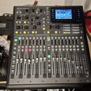 Digitální mixážní pult černé barvy s nápisem X32 PRODUCER a logem Behringer. Zařízení obsahuje displej, zahlreiche posuvníky, tlačítka a otočné ovlad…