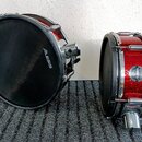 Dvě elektronické bubny v červené barvě s glitrovým povrchem a chromovanými obručemi. Na černém membránovém povrchu levého bubnu je bílý nápis ALESIS.…