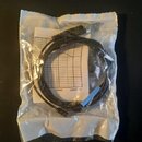 Černý audio kabel s konektorem typu jack, sbalený do kroužku a umístěný v průhledném plastovém sáčku. Pod kabelem je vidět bílý papír s grafem a nápi…
