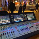 Digitální mixážní pult stříbrné barvy s černým rámem. V pravém horním rohu je nápis Soundcraft Vi2000. Zařízení obsahuje tři barevné displeje s grafi…