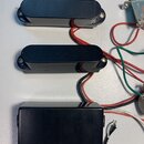Tři černé elektrické snímače s kovovými kryty a připojeným barevným kabelážím. Dva horní mají zaoblený obdélníkový tvar, spodní je hranatý. Na povrch…