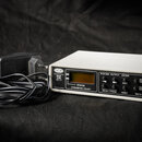 Bílý obdélníkový přístroj s nápisy MXC-200 a MIDI to DMX-512 Converter. Na předním panelu je malý displej, čtyři tlačítka a nápisy SYSTEM, OUTPUT, EN…