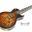 Elektrická kytara s tvarem Les Paul, s plameníkovým topem v hnědé barvě a zlatým hardwarem. Na těle jsou dva humbuckery, čtyři ovládací knofíky a pře…