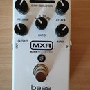 Bílý efekt pedál s nápisem bass compressor. Na horní části jsou čtyři černé ovládací knoflíky s popisky RELEASE, RATIO a ATTACK a stupnicí GAIN REDUC…