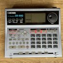 Stříbro-černý rytmický automat značky BOSS, model Dr.Rhythm DR-880. Zařízení obsahuje displej, ovládací knofíky a množství gumových padů s popisy jak…