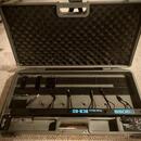 Otevřený šedý plastový kufr s černou pěnovou výplní. Uvnitř je umístěna černá pedálboard s nápisem BOSS Pedal Board BCB-60. V kufru jsou dále umístěn…