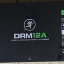 Zadní strana černého reproduktoru s nápisy DRM12A a 2000W 12" ARRAYABLE POWERED LOUDSPEAKER. Jsou zde vidět konektory INPUT a OUTPUT, přepínač PARALL…