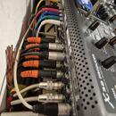 Detailní pohled na zadní panel černého míchacího pultu s nápisem T32 PRODUCER a textem presented by GTOPS. Do zařízení jsou zapojeny různé typy kabel…