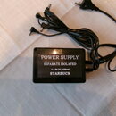 Černý napájecí adaptér s nápisy POWER SUPPLY, SEPARATE ISOLATED, 4 x 9V DC/100mA a STARBUCK. Z přístroje vychází kabel s čtyřmi konektory pro napájen…