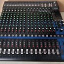 Černý mixážní pult značky YAMAHA, model MG20XU. Zařízení obsahuje řadu vertikálních faderů s bílými krytkami a červenými prvky, množství regulačních…