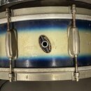 Fotografie znázorňuje buben s modro-žlutým přechodovým povrchem. Uprostřed korpusu je oválný štítek s nápisem „Quality Slingerland DRUMS CHICAGO, ILL…