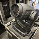 Černý movable head reflektor umístěný v transportním kufru s pěnovou výplní. Zařízení má matný plastový povrch a velkou přední čočku. Na boku jsou vi…