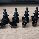 Šest kusů ladících mechanismů v černé barvě s kovovým povrchem. Jsou uspořádány v řadě na světlém dřevěném povrchu. Na mechanismech nejsou viditelné…