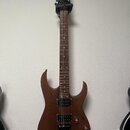 Elektrická kytara s hnědým dřevěným povrchem těla a hnedou hmatnicí. Na hlavě je bílý nápis Ibanez. Kytara má tři černé humbuckery, jeden ovládací kn…