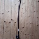 Na fotografii je smyček z tmavého dřeva s černou rukojetí. V dolní části je vidět kovový mechanismus pro napínání vlasí a malý stříbrný štítek s neči…