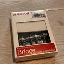 Krabice s kytarovým kobylníkem v kovovém provedení. Na obalu je červený nápis Bridge, text Electric Guitar & Bass a webová adresa www.g-gotoh.com. V…