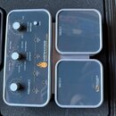 Šedý efekt pedál s nápisy HOTHAND MOTION CONTROLLED WAH FILTERS a SOURCE AUDIO. Zařízení obsahuje dva bílé otočné knoflíky s popisky STRUM a FREQUENC…